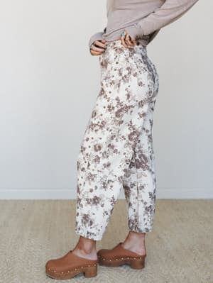 A side-profile shot of floral barrel-leg jeans in cream and dusty mauve, styled with a soft taupe long-sleeve top and studded wood clogs — the kind of outfit that looks effortless but clearly wasn't an accident.