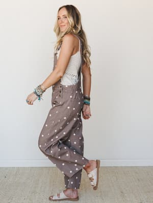 A sun-warmed model walks mid-stride in polka dot barrel-leg overalls layered over a crochet cami, stacked with colorful bracelets and rings — the kind of outfit that looks like it just happened and somehow works perfectly.