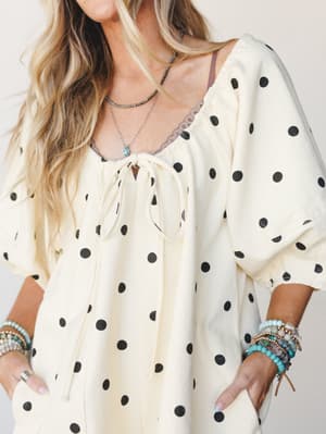 A cream polka dot romper styled with layered boho jewelry and stacked beaded bracelets — easy and expressive, like something you'd throw on and immediately feel like yourself in.