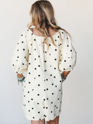 A cream and black polka dot romper shot from the back, styled with stacked turquoise and beaded bracelets — relaxed and playful with a retro-boho ease.