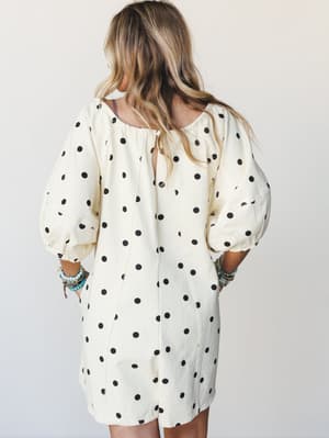 A cream and black polka dot romper shot from the back, styled with stacked turquoise and beaded bracelets — relaxed and playful with a retro-boho ease.