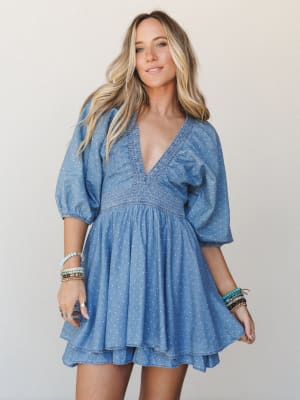 A breezy denim mini dress with polka dots and a smocked waist gives off that perfect 'I got dressed effortlessly but actually thought about it' energy — styled with stacks of beaded bracelets and a relaxed, confident smile.