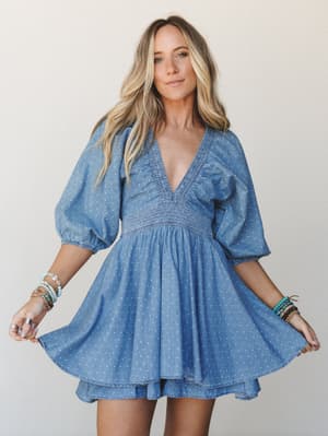 A breezy polka dot denim mini dress with billowy puff sleeves and a smocked waist, styled with stacked turquoise and beaded bracelets — the kind of dress that makes a Tuesday feel like something worth dressing for.