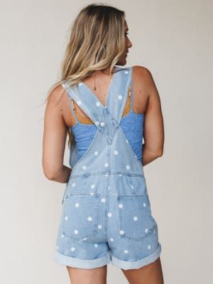 A back view of polka dot denim short overalls styled over a blue lace cami, with crossback straps and rolled cuffs — playful and warm-weather-ready in the best possible way.