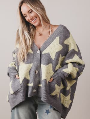 Woman wearing a gray cardigan with star patterns on a plain background