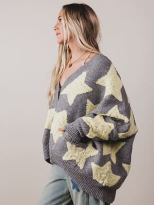 Woman wearing a gray sweater with star patterns on a plain background
