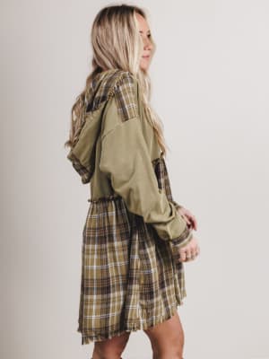 Woman wearing a green jacket over a plaid dress on a plain background