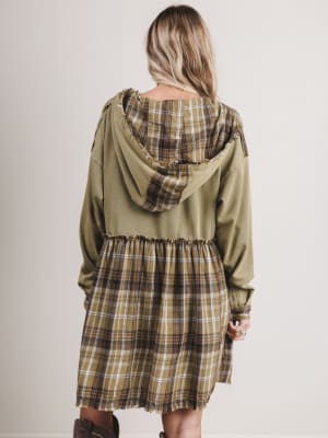 Person wearing a plaid dress with an olive green hooded jacket on a plain background