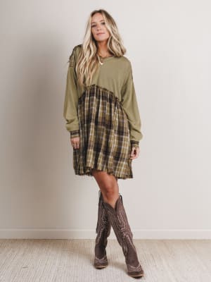 Woman wearing a green dress with plaid pattern and brown cowboy boots against a plain background