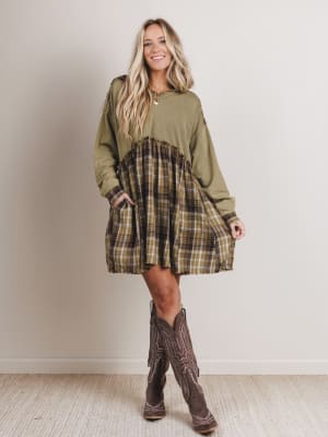Woman wearing a green dress with plaid skirt and brown boots against a plain background
