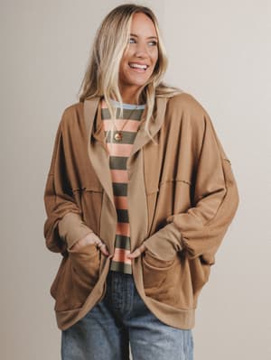 Woman wearing a brown jacket over a striped shirt with a neutral background