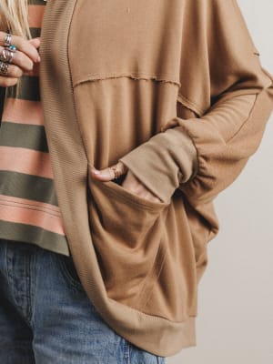 Person wearing a brown oversized sweater with a neutral background