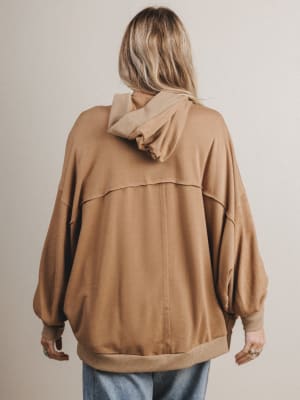 Person wearing a brown jacket with a hood on a plain background