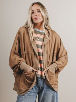 Woman wearing a brown jacket over a striped shirt with a neutral background