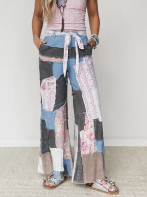 Wide-leg patchwork pants in a mix of washed denim, floral cotton, and vintage-feeling fabrics — styled with a cropped pink lace top, beaded sandals, and layered jewelry for an effortlessly lived-in boho look.
