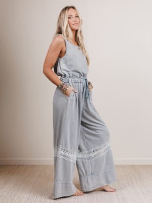 Woman wearing a light gray jumpsuit with lace details on a plain background