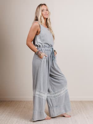 Woman wearing a light gray jumpsuit with lace details on a plain background