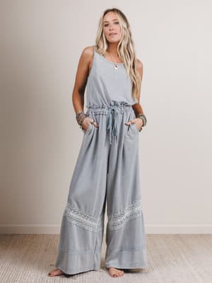 Woman wearing a light gray jumpsuit with lace details on a plain background