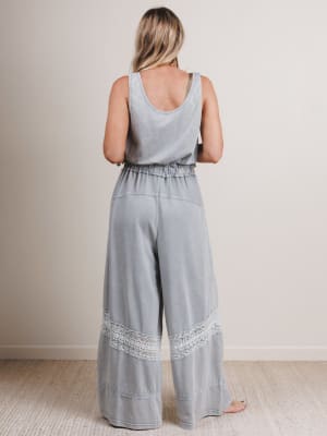 Woman wearing a light blue jumpsuit with lace details on a plain background