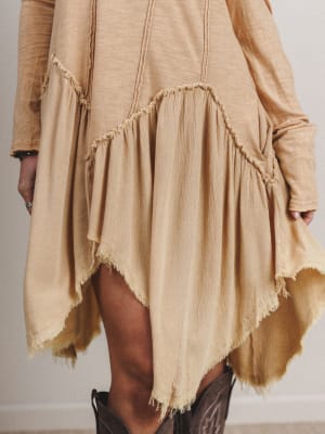 Beige dress with frayed hem and brown boots on a neutral background