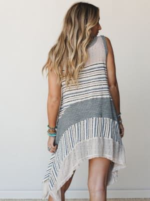 A breezy mixed-knit tunic shot from behind, with an asymmetric handkerchief hem and effortless stripe patchwork — the kind of piece that looks like it's already been on three beach trips and somehow gets better every time.