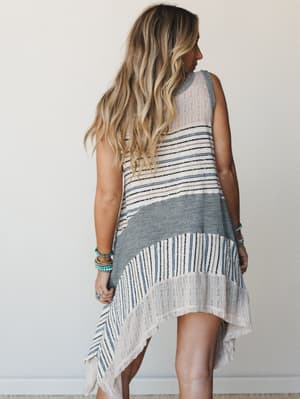 A breezy mixed-knit tunic shot from behind, with an asymmetric handkerchief hem and effortless stripe patchwork — the kind of piece that looks like it's already been on three beach trips and somehow gets better every time.