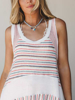 A close-up torso shot of a multicolor striped knit tunic layered over a blush pink top, styled with a starfish charm necklace — the kind of effortless summer look that feels like it was put together at a beach house.
