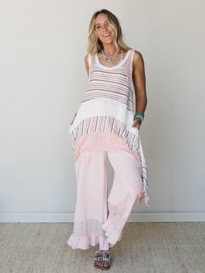 A striped knit tunic with an asymmetric handkerchief hem is layered over blush wide-leg pants with eyelet trim — the whole look has that effortless, sunny energy of someone who just got back from somewhere good.
