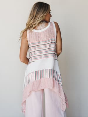 A model shot from behind showcasing a mixed-texture sleeveless knit tunic with a dramatic handkerchief hem, styled with soft blush wide-leg pants — the kind of outfit that feels like a vacation you're still thinking about.