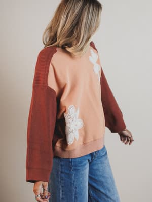 Person wearing a brown sweater with floral patterns on a plain background