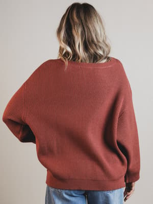 Person wearing a rust-colored sweater against a plain background