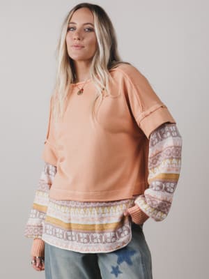 Woman wearing a peach-colored sweatshirt with patterned sleeves against a plain background