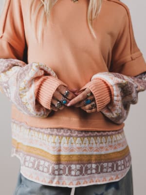 Person wearing a patterned sweater over a plain top with a neutral background