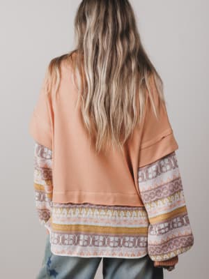 Person wearing a peach-colored top with patterned sleeves on a plain background