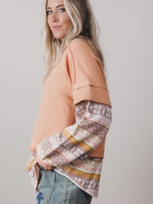 Woman wearing a peach-colored top with patterned sleeves against a plain background