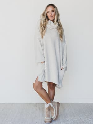 Woman wearing a light gray poncho and boots against a white background