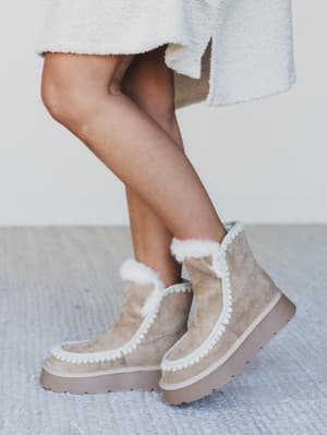 Beige winter boots with white fur trim worn indoors on a light-colored rug.