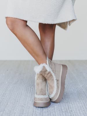 Person wearing beige suede boots with fur trim on a light background
