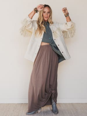 Woman wearing a white fringed jacket, green sweater, and brown pants against a white background