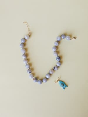 A grey marbled stone bead necklace laid flat with a detached turquoise fish charm pendant beside it — earthy, collected, and quietly coastal.