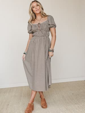 A gingham midi dress in warm brown and cream does all the right things — puff sleeves, a gathered waist, and a keyhole neckline that feels like a farmhouse fairytale, styled with tan mules and stacked boho bracelets.