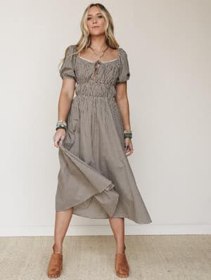 A midi dress in brown gingham with puff sleeves and a gathered waist gives off effortless countryside-meets-boho energy, styled with tan clogs and stacked bead bracelets for a look that feels genuinely lived-in.