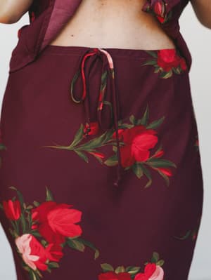 A close-up detail shot of a wine-colored floral skirt with a delicate self-tie waist closure, layered over a matching ruffled top — moody, romantic, and made for a fall evening out.