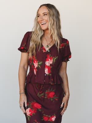 A matching floral set in deep wine — the kind of outfit that looks like it was made for a dinner reservation you're actually excited about, worn here with layered gold jewelry and an effortless smile.