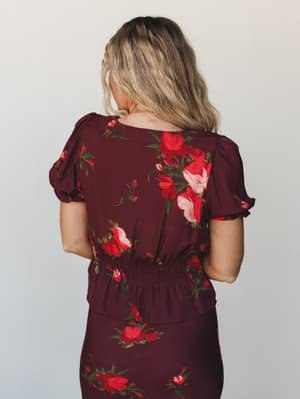 Shot from the back, a floral wine blouse with puff sleeves and a smocked waist sits over a matching skirt — romantic and a little moody, like something you'd wear to a fall dinner and feel really good about.