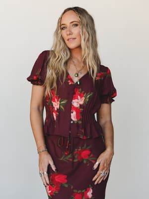 A flowy wine-toned floral blouse paired with a matching skirt, styled with layered gold jewelry and stacked rings — the kind of outfit that feels dressed up without trying too hard.