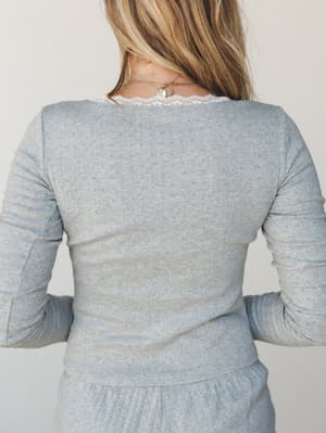 A back-view shot of a heather grey pointelle knit long-sleeve top with a delicate lace neckline trim peeking through, styled as a matching set with coordinating ribbed bottoms — soft, lived-in, and quietly pretty.
