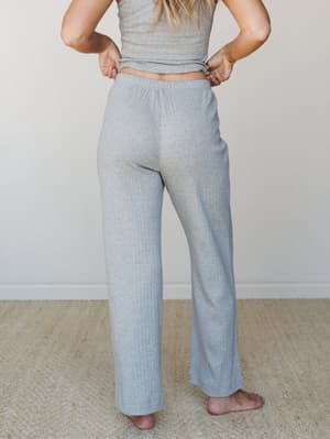 Shot from behind, a model shows off wide-leg ribbed pants in heather grey paired with a matching crop top — the kind of easy two-piece set that makes staying in feel intentional.