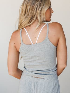 Shot from the back, a model wears a heather grey pointelle knit cami with thin spaghetti straps over a white bralette, paired with matching grey ribbed bottoms — soft, relaxed, and the kind of set you reach for on a slow morning.