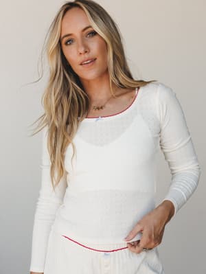 A cream pointelle long-sleeve top with red contrast stitching at the neckline and hem, styled with matching cream bottoms — soft, nostalgic, and cozy in the best pajama-set-you'd-actually-wear-out kind of way.